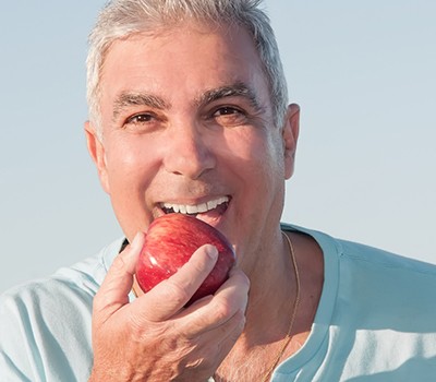man having an apple and enjoy the everyday benefits of dental implants in Mayfield Heights